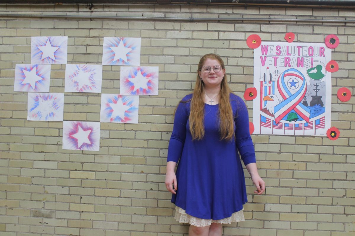 Mrs. Bailey standing next to student work for Veterans Day program 2023.